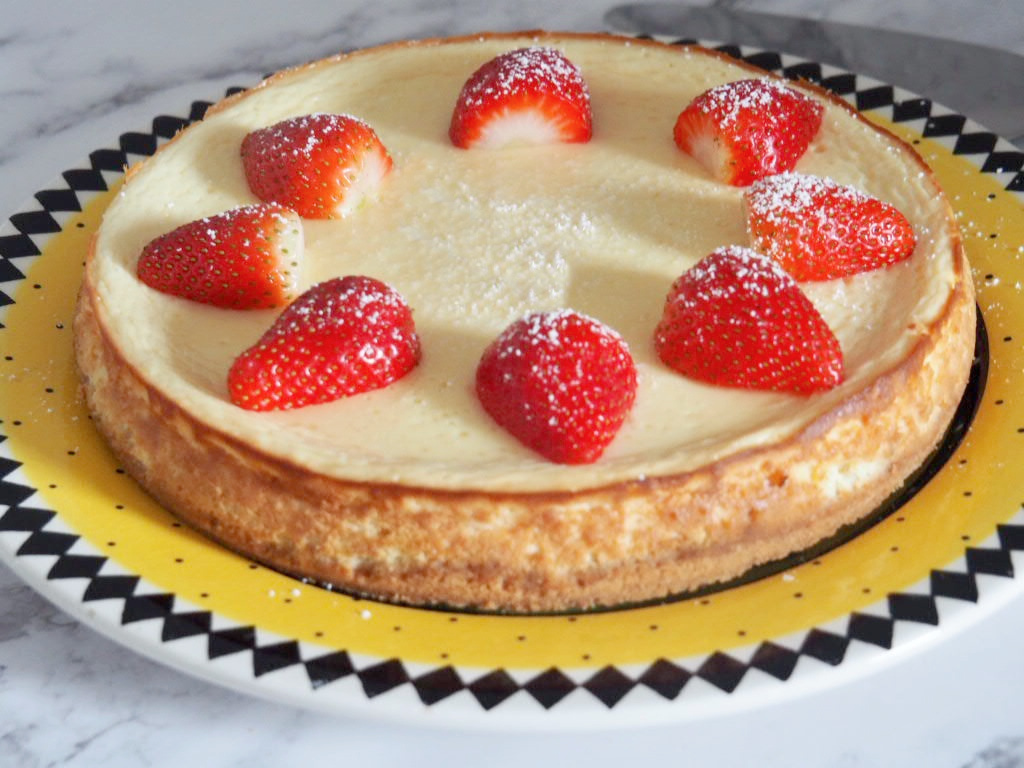 light and luscious lemon baked cheesecake decorated with halved strawberries on yellow plate