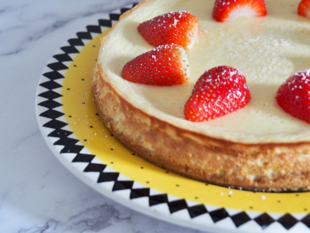 side view of lemon cheesecake decorated with halved strawberries on a yellow plate