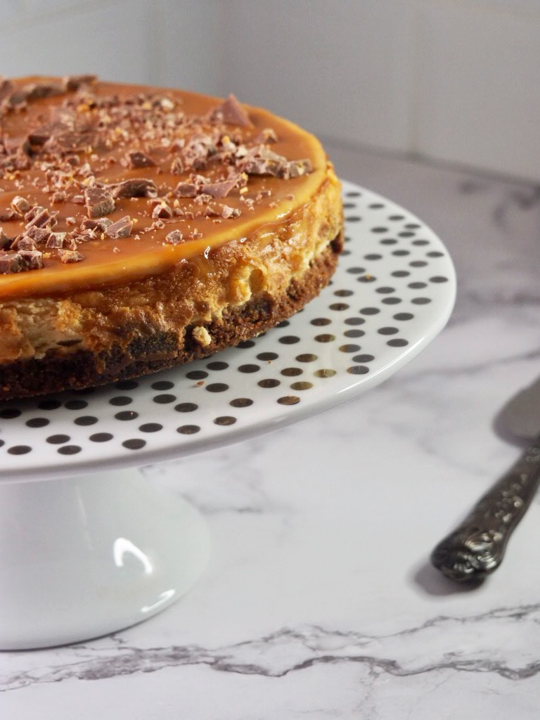 side view of salted caramel cheesecake on a white and silver spotted cake stand