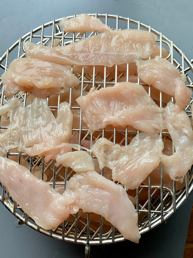 thinly sliced chicken ready to dehydrate on dehydrating racks
