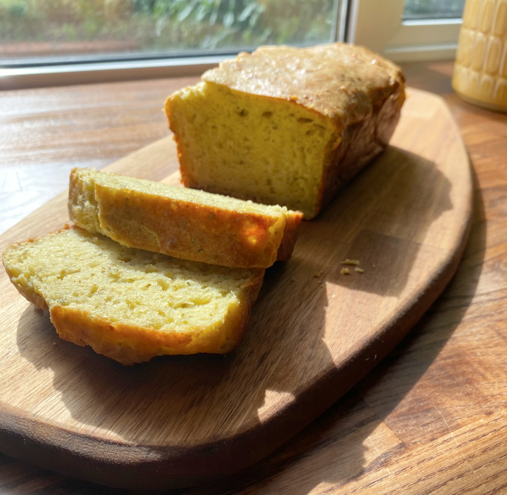 pesto loaf with a few slices  cut on a wooden chopping board in front of a sunlit window