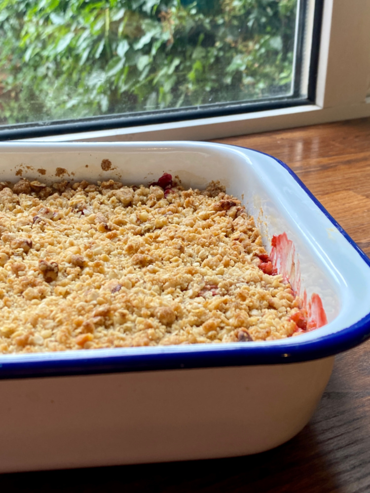 a tray of rhubarb crumble on a wooden bench in front of a sunlit window