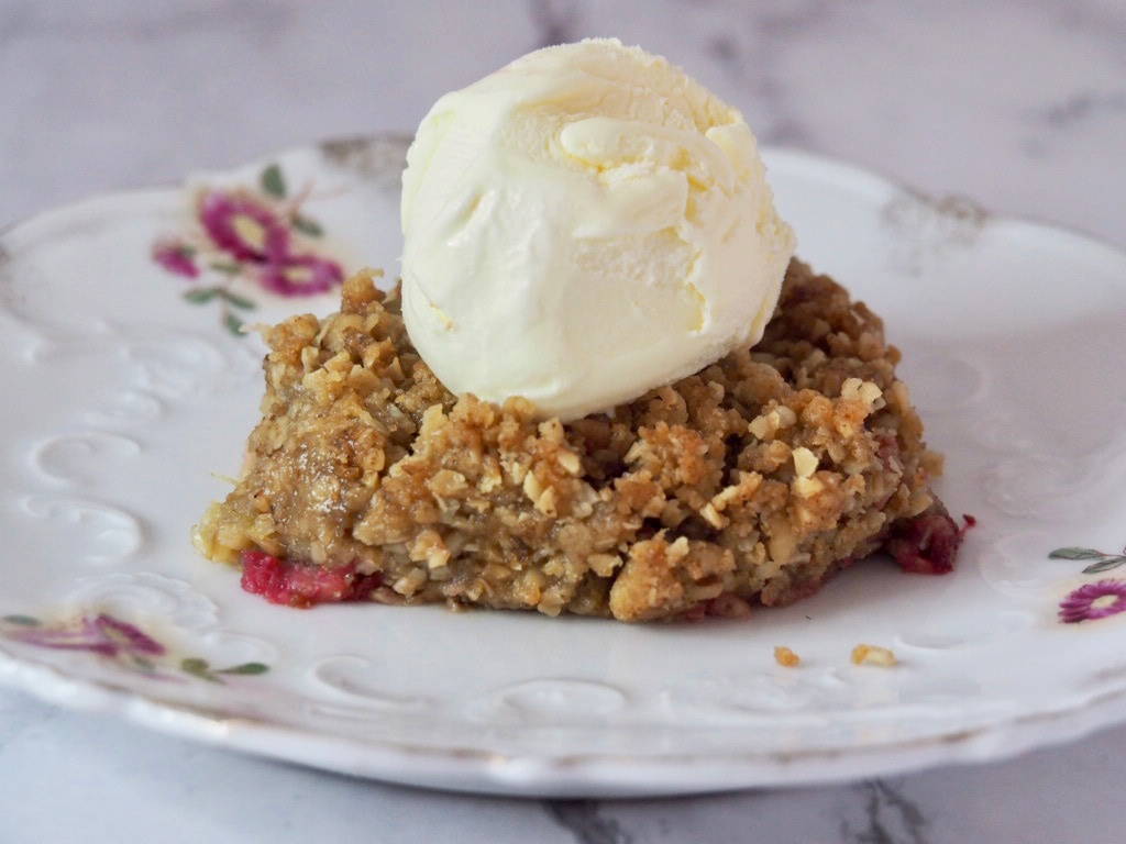 A piece of rhubarb crumble on a small vintage plate with a scoop of ice cream on top.