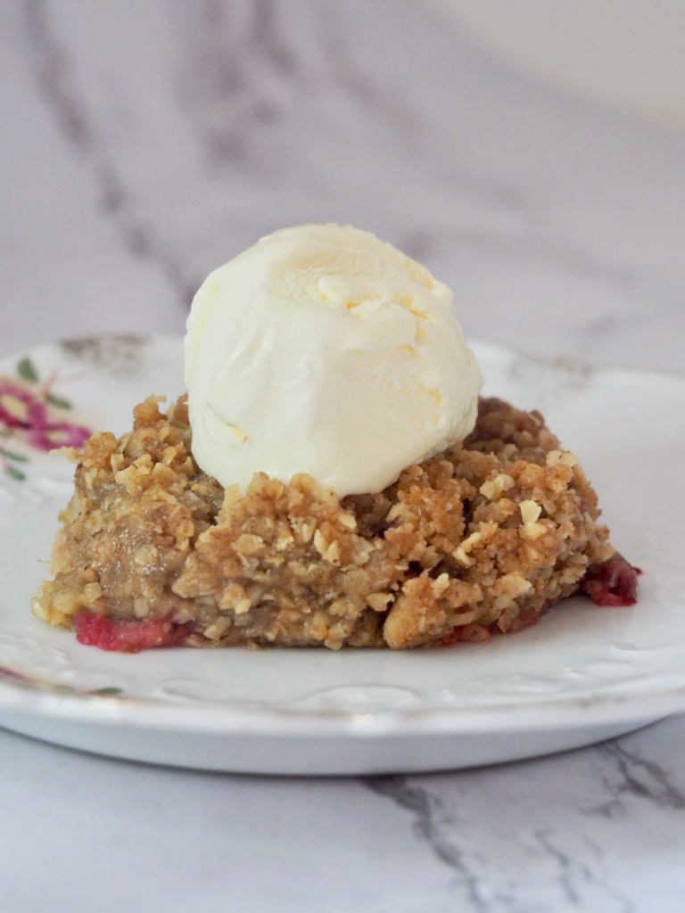 a piece of rhubarb crumble topped with a scoop of vanilla ice cream on a small vintage plate