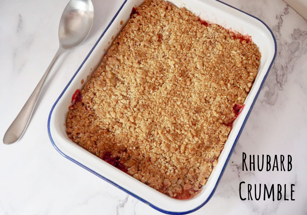 looking down on a tray of rhubarb crumble. A large serving spoon is next to it.