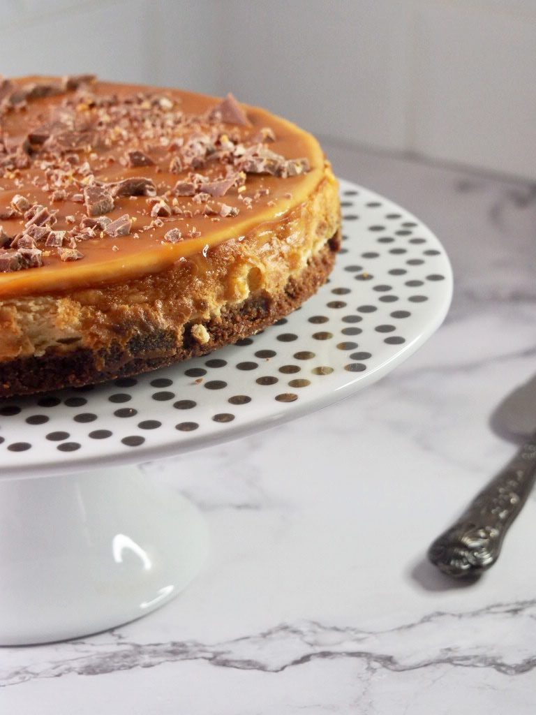 side view of salted caramel cheesecake on a white cake stand