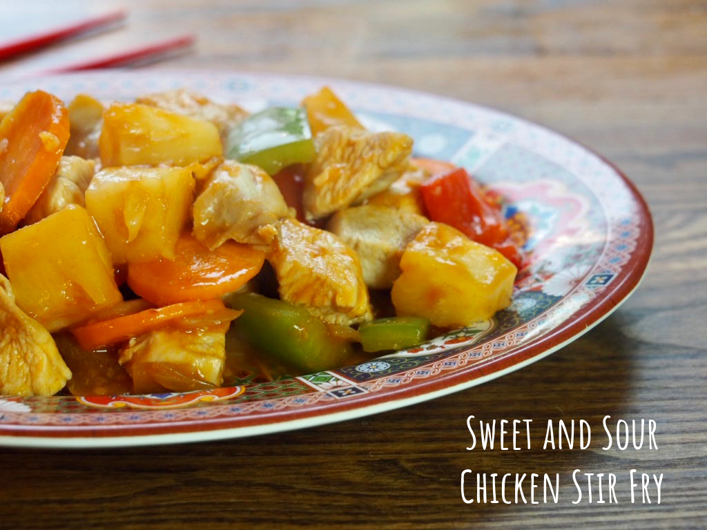 sweet and sour chicken stir fry on a chinese oval patterned plate on a wooden background next to a pair of red chopsticks