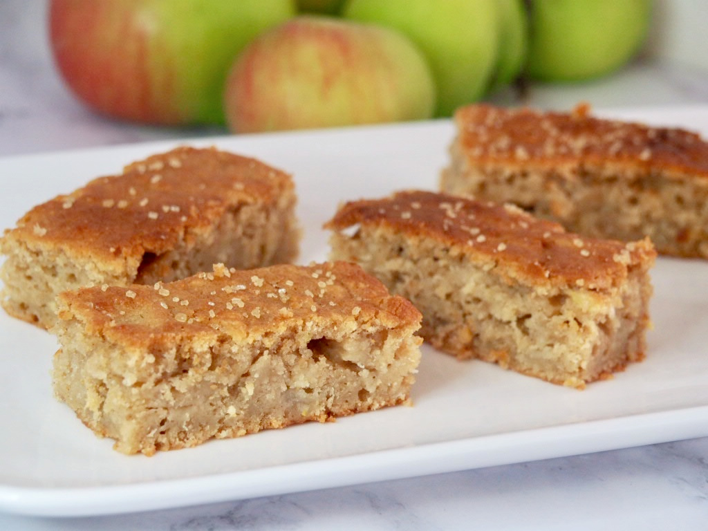 a plate of cake slices with some apples in the background