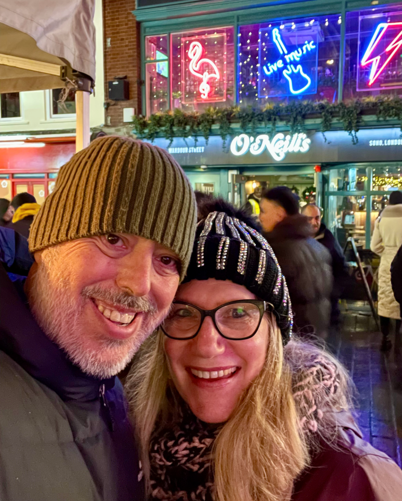a man and woman both wearing beanies standing on a busy street in front of a neon sign