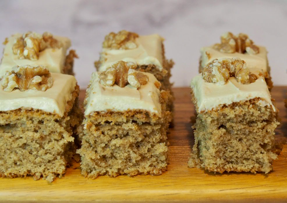 squares of coffee cake topped with fudge icing and walnut pieces on a wooden board