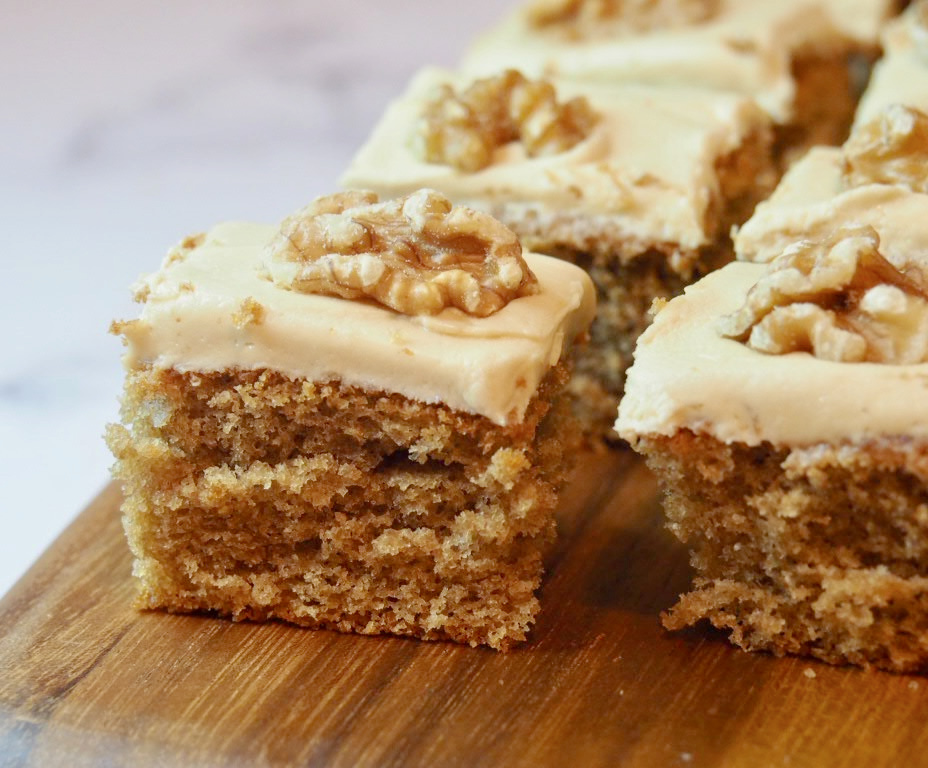 looking side on at squares of coffee sponge topped with fudge icing and topped with walnuts on a wooden board
