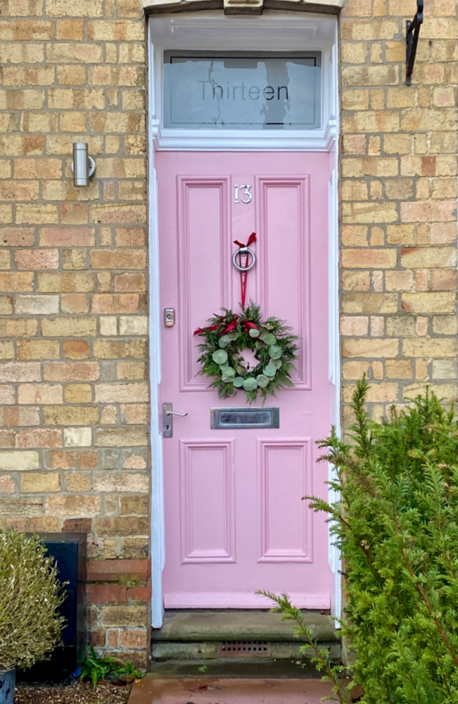 a baby pink front door with a christmas wreath hanging on it by a red ribbon