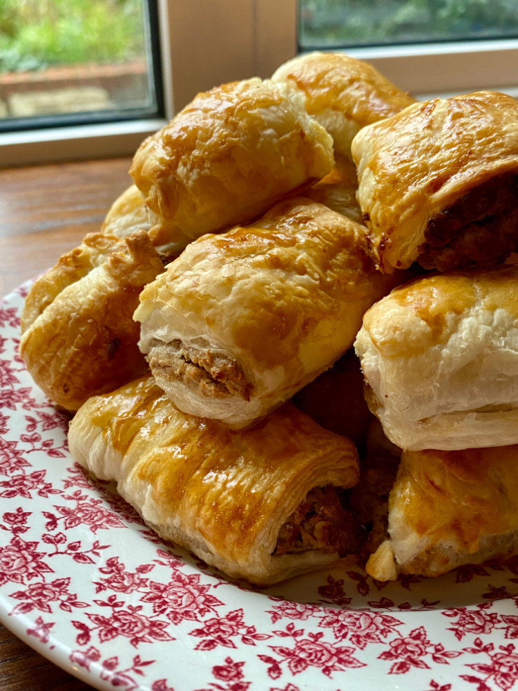 a plate of vegetarian sausage rolls. The plate is white with a pink floral pattern and it's positioned in front of a window.